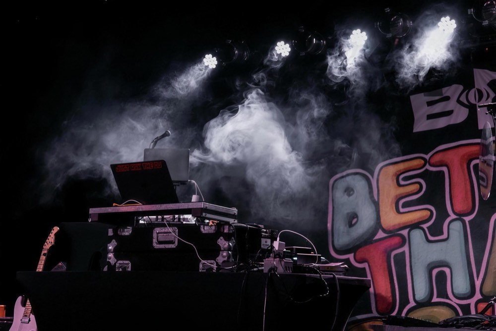 DJ at the decks with smoke and white stage lights behind him