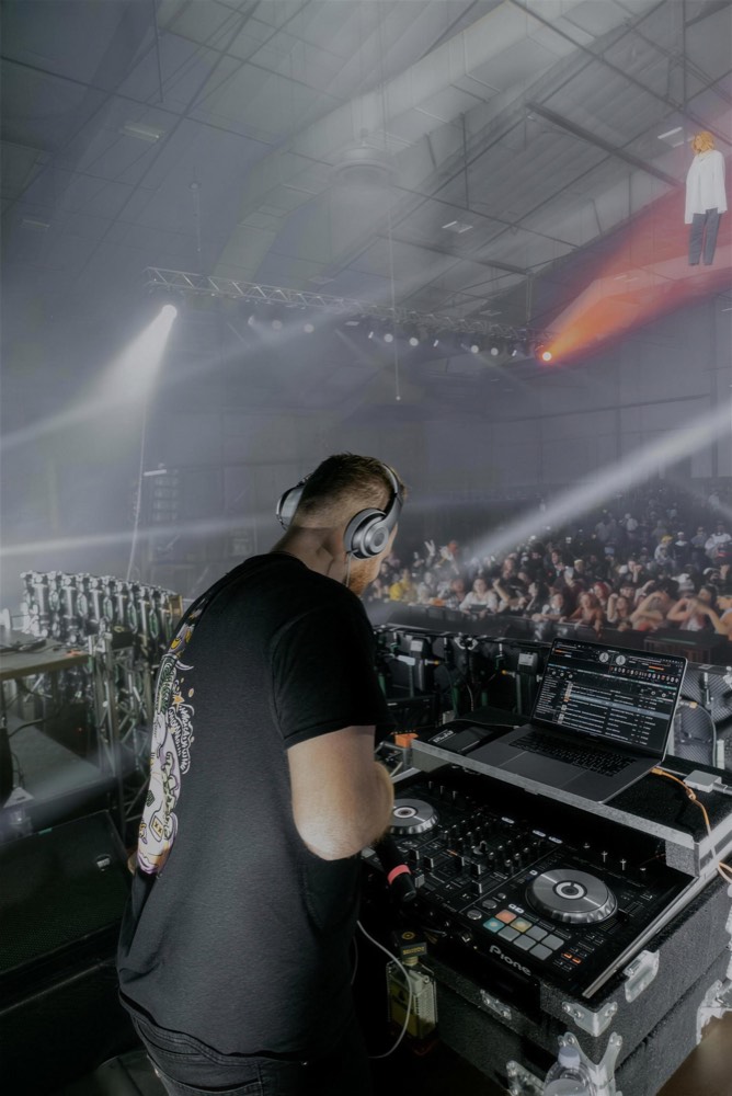 DJ seen from above at the decks, playing to a crowd through haze