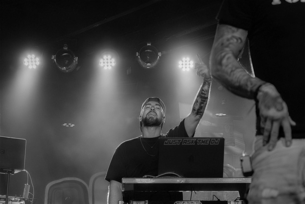 Black and white photo of a DJ at the decks under a row of stage lights