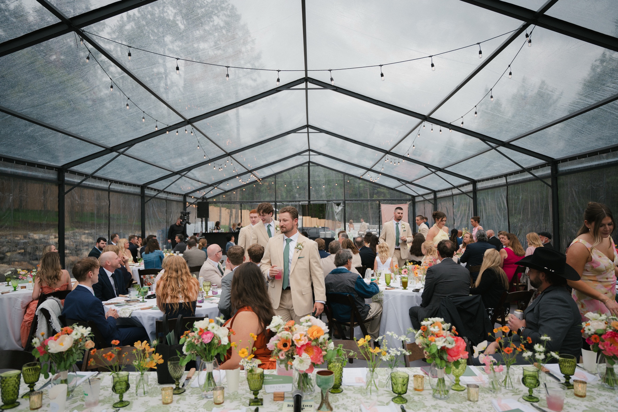 Guests seated at flower-filled reception tables under a clear tent