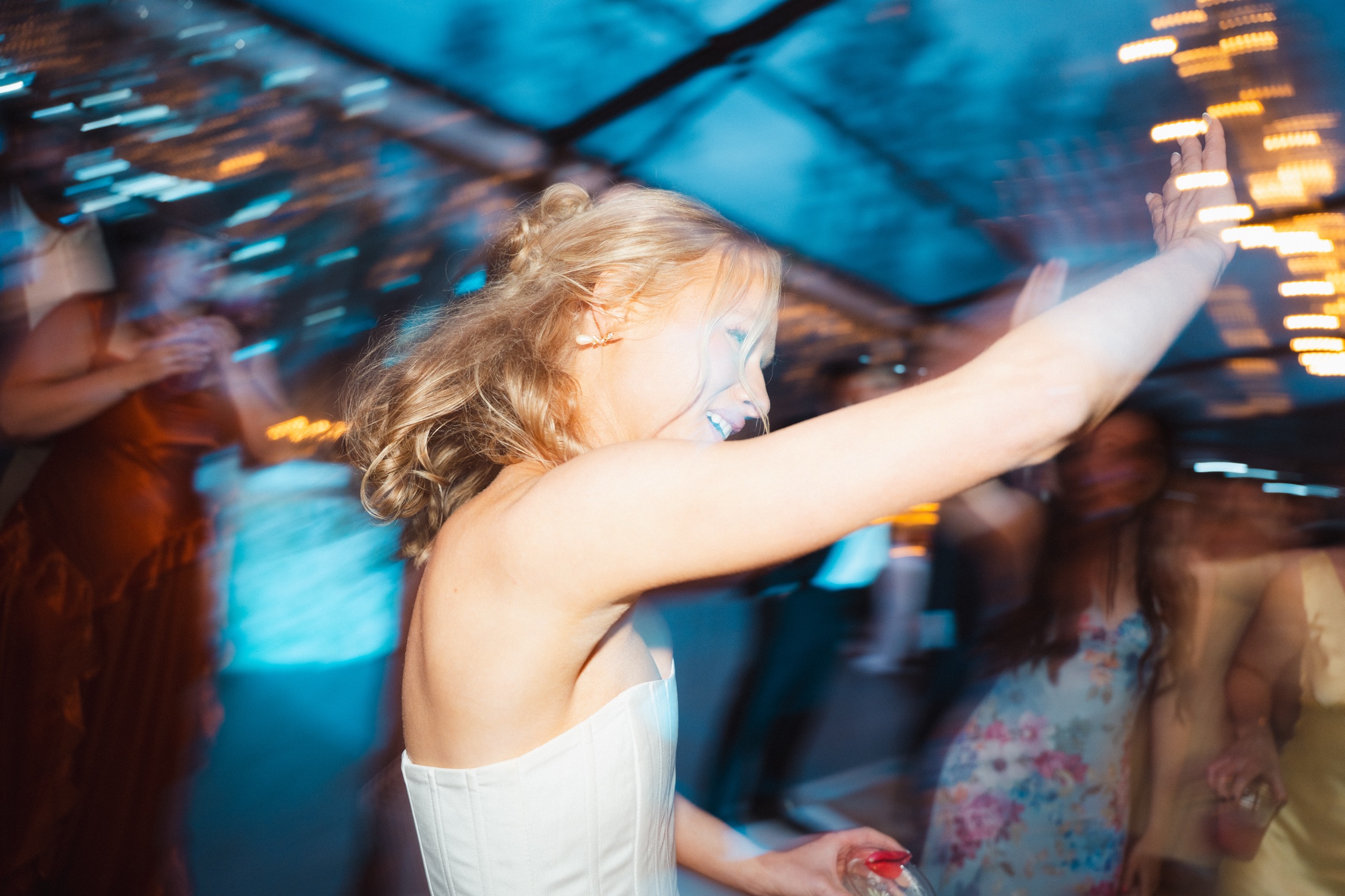 Bride dancing with one arm raised, lights streaking behind her
