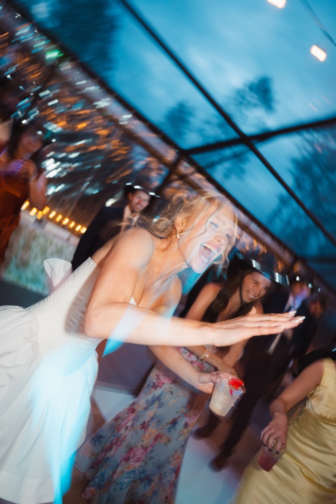 Bride laughing mid-dance with guests around her
