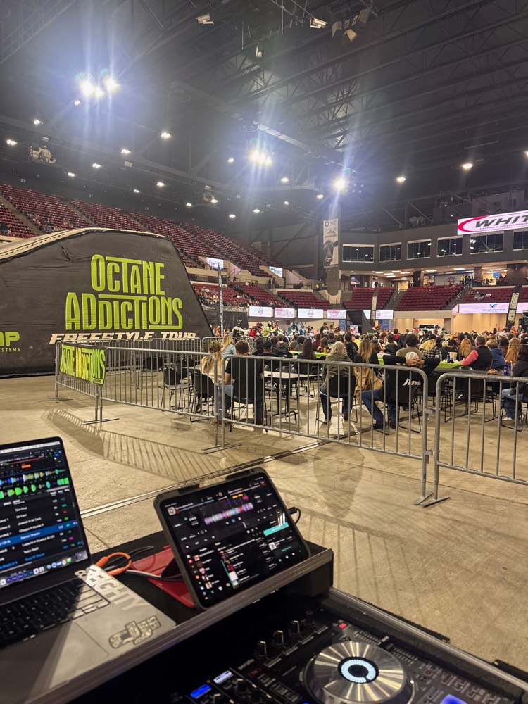 Arena floor with a crowd behind barricades, seen from the DJ booth