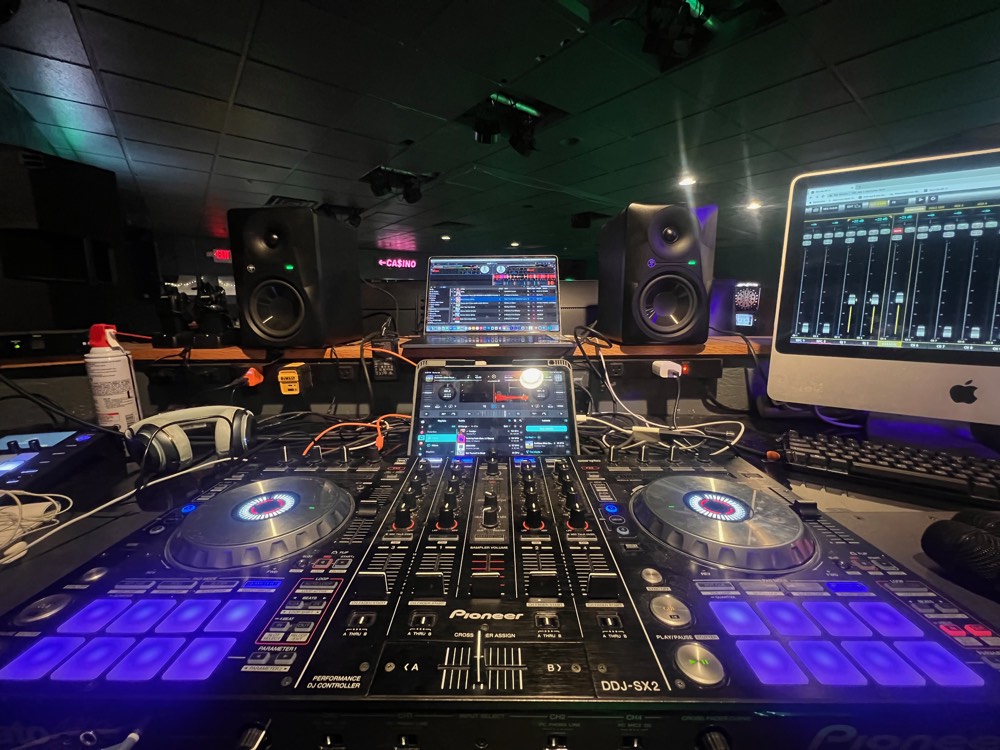 Two DJ controllers and monitors under blue light