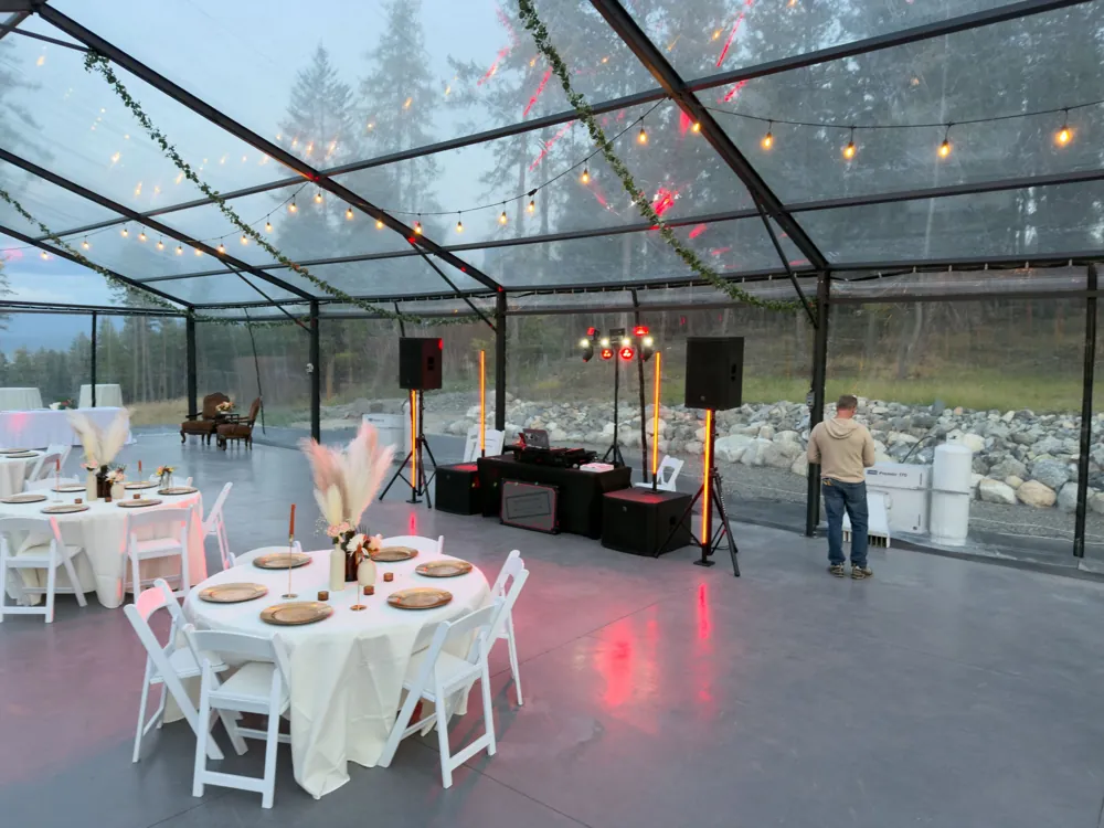 Reception tables with gold chargers and pampas centerpieces facing the DJ setup under string lights