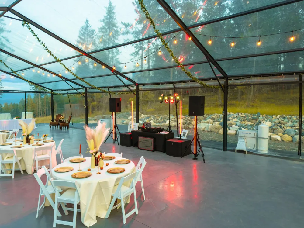 Reception tables with gold chargers and pampas centerpieces facing the DJ setup under string lights