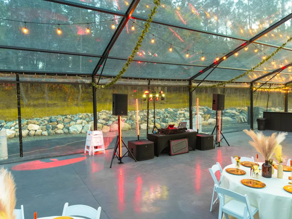 Reception tables with gold chargers and pampas centerpieces facing the DJ setup under string lights