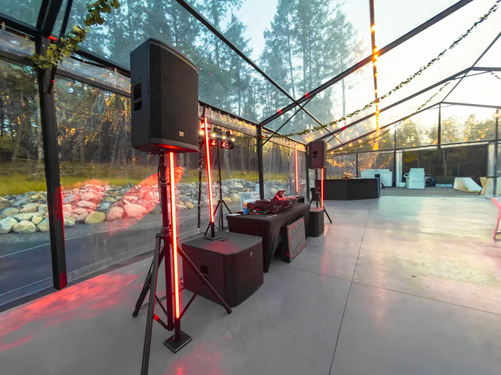 DJ speakers and glowing red LED pillars at golden hour inside a clear wedding tent